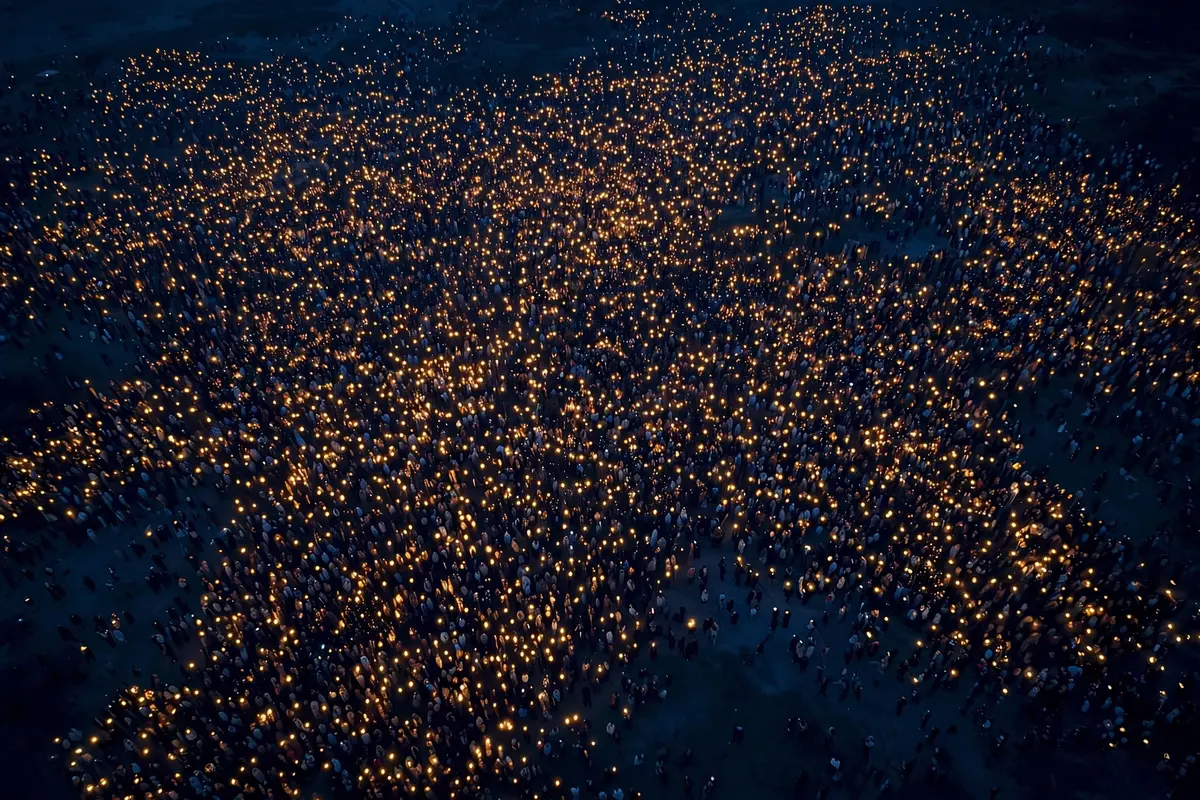 A vast crowd at dusk holding small warm lights, seen from above